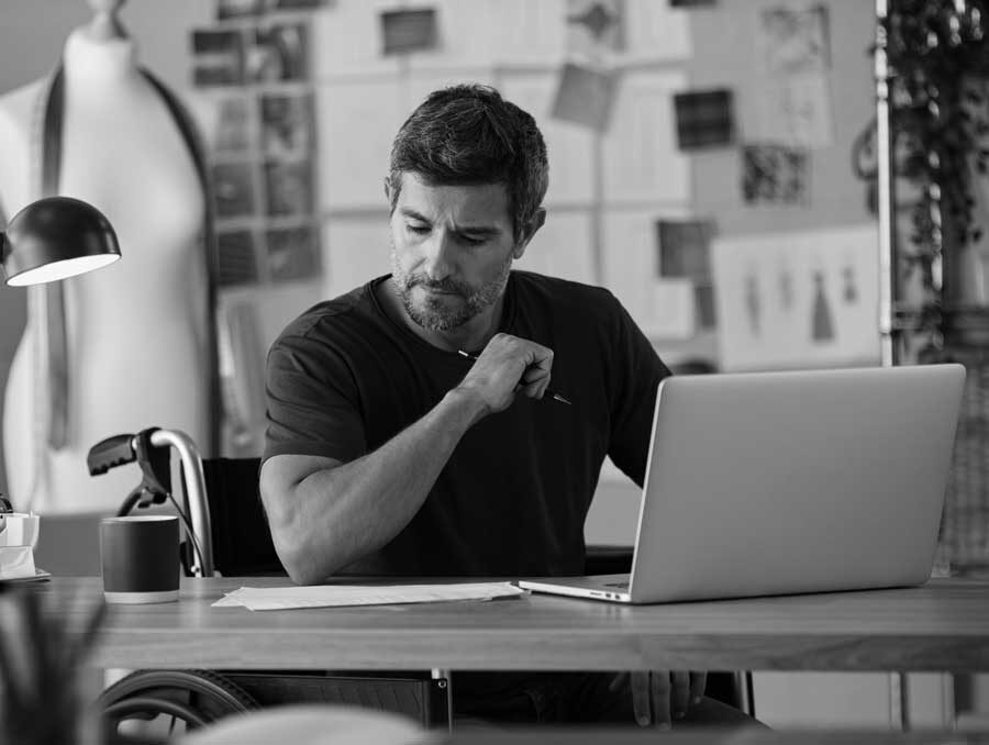 Man i rullstol arbetar vid skrivbord. Foto: Envato|
