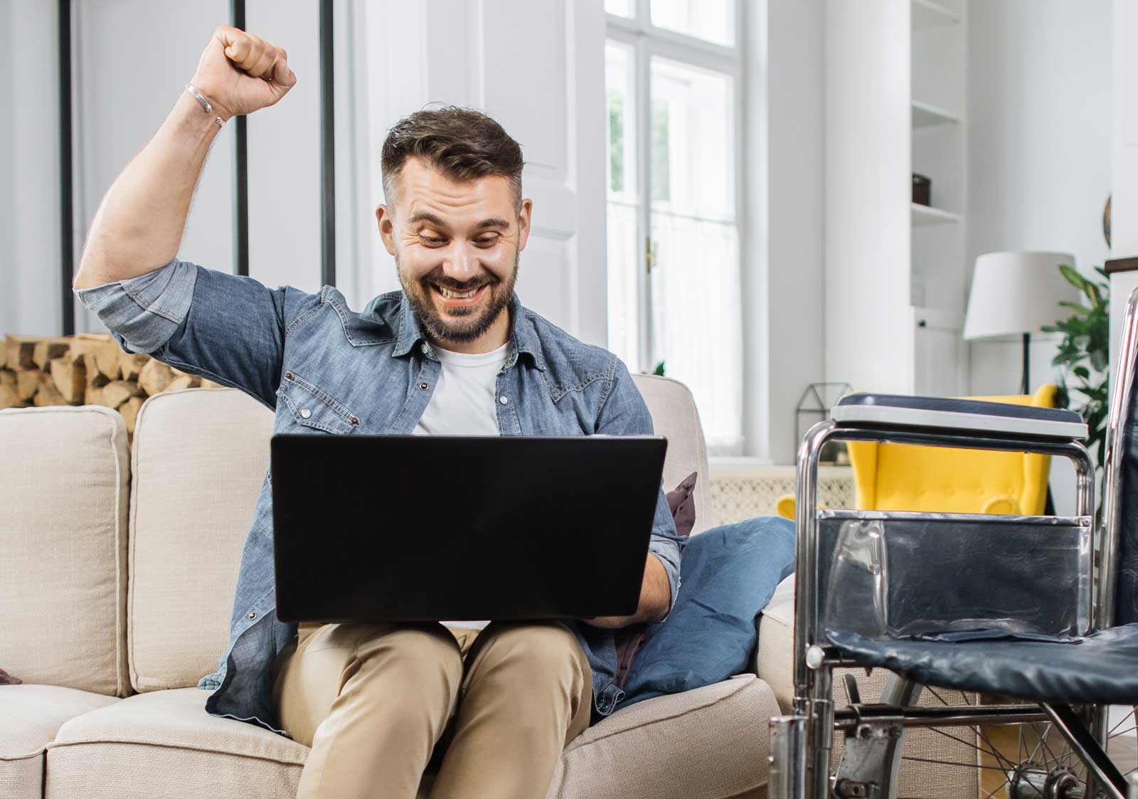 Man med dator i soffa och rullstol bredvid. Foto: Envato